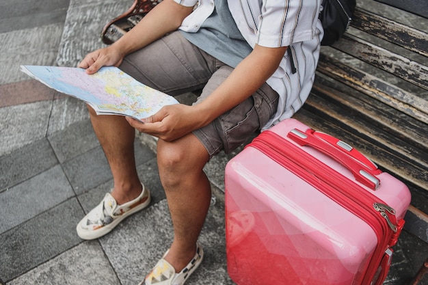 Close-up of male traveler hands sitting at the chair with suitcase and holding map.