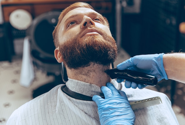 Close up man getting hair cut at the barbershop wearing mask during coronavirus pandemic. Professional barber wearing gloves. Covid-19, beauty, selfcare, style, healthcare and medicine concept.