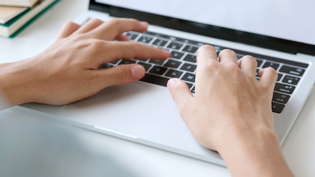 Photo close up of man hand typing laptop computer while working at home office, student college online study, learning, people and technology