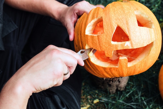 A close up of man hands who cuts with knife a pumpkin as he prepares a jack-o-lantern.