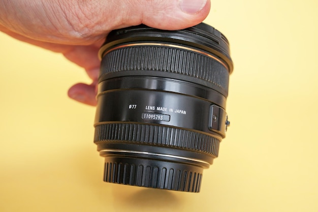 Close-up of a man holding a camera lens in his hand on a yellow background.