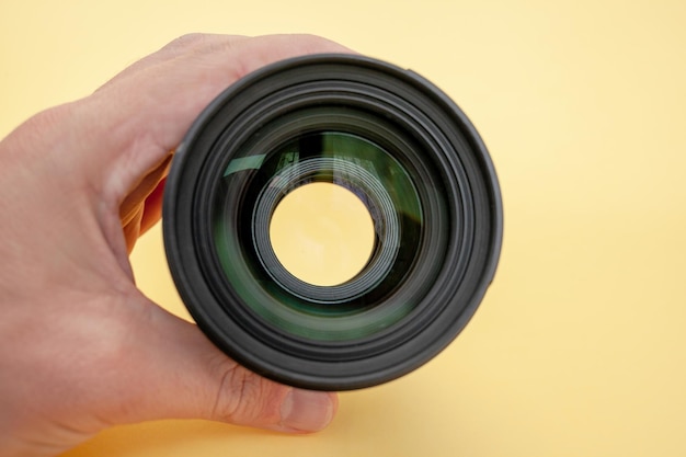 Close-up of a man holding a camera lens in his hand on a yellow background.