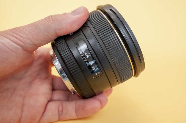 Close-up of a man holding a camera lens in his hand on a yellow background.