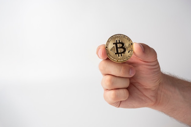 Close-up of a man holding a gold-colored bitcoin coin. White background, Cryptocurrency Concept, copy space