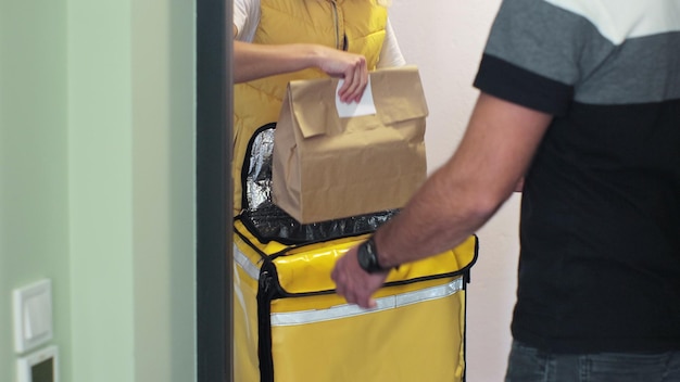 Close up man opens door to food delivery woman taking order out of thermal insulated bag and giving it to male customer View from the apartment Inside shot Food delivery concept