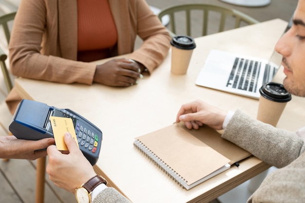 Close-up of man paying for coffee with credit card while having a meeting with his partner in cafe