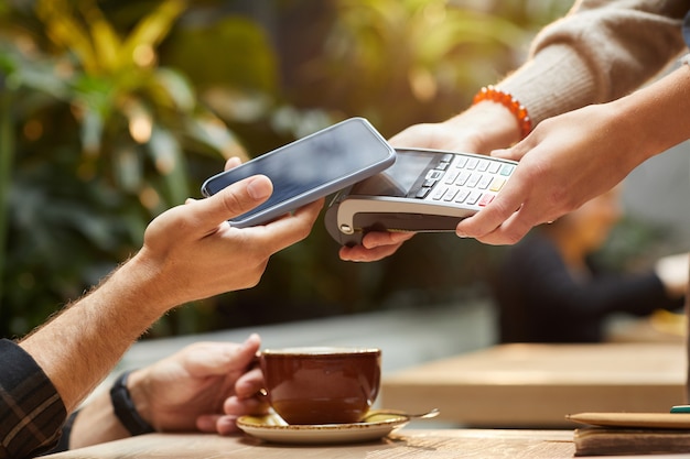 Close-up of man paying online with mobile phone for his order in cafe