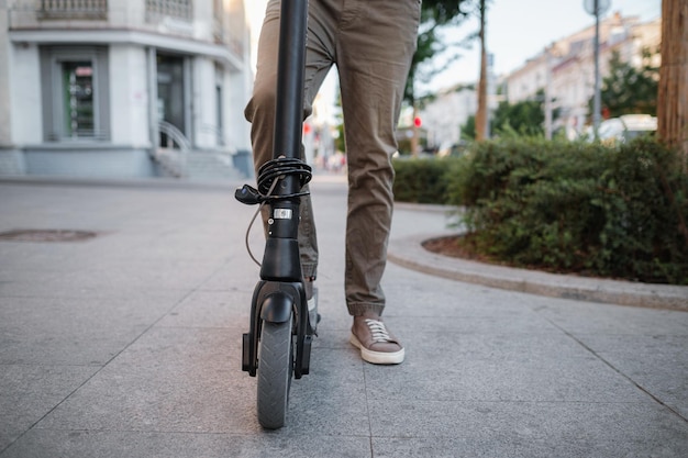 Close up of man riding black electric kick scooter at cityscape at sunset