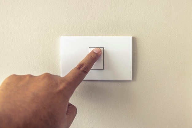 Close up Man's fingers are turning on or off a white light switch on a cream colored wall at night at home Energy safety save electricity copy space