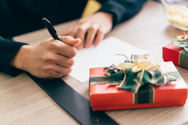 Close up man's hand is writing on a blank Christmas postcard with a pen Couple sitting and writing Christmas card together for sending with surprise gifts at home during Christmas holiday