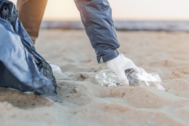 Close up of man's hand picking up trash and plastics cleaning the beach with a garbage bag