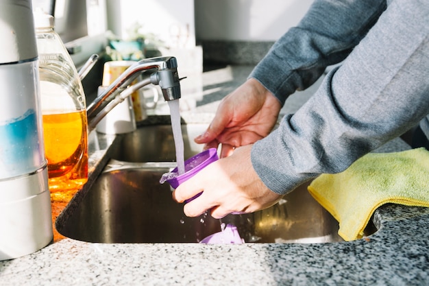 Close-up of a man's hand washing container in kitchen sink