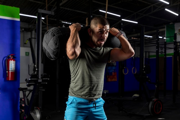 Close up of a man in sportswear in a gym doing squats with a sandbag on his back