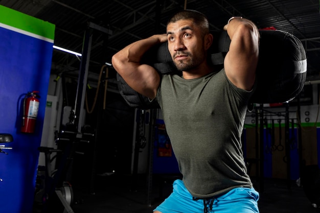 Close up of a man in sportswear in a gym doing squats with a sandbag on his back