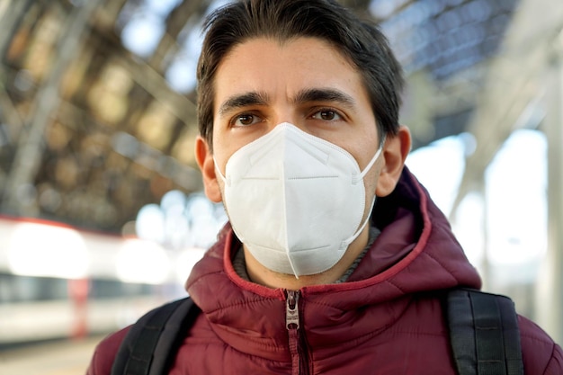 Close up of man wearing protective mask FFP2 KN95 at train station staring away Blurred background