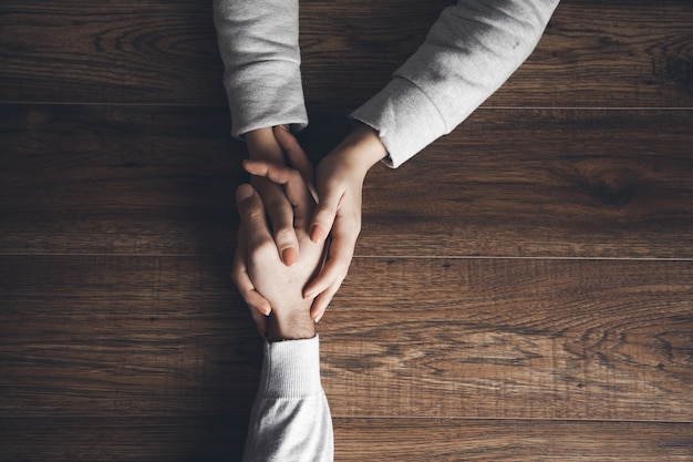 Close up on a man and a woman holding hands at a wooden table