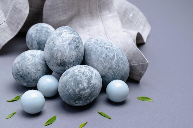 Close-up of marble-colored Easter eggs with green leaves and a napkin on a gray background. Easter background.