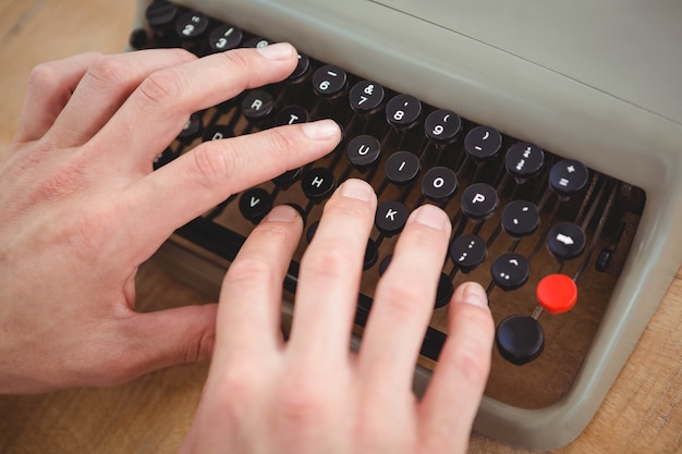 Close up of masculine hands typing on old typewriter on wooden table