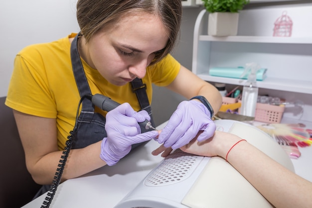 Close-up of a master girl doing a manicure to a client using a manicure machine. A manicurist works with an electric nail drill in a beauty salon. Hardware process of manicure.