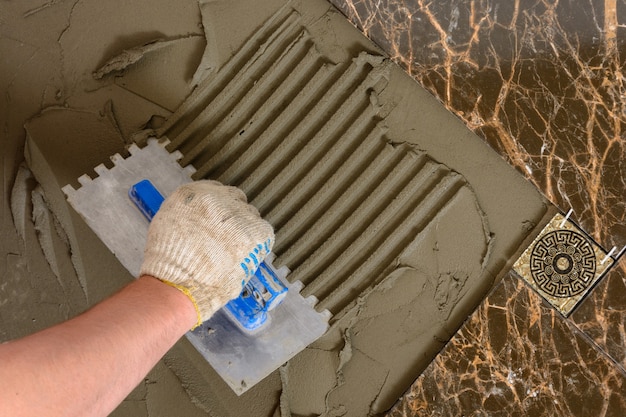 Close-up of a master's hand that makes furrows in a glutinous solution for laying marble tiles