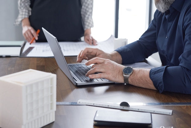 Close-up of mature businessman sitting at the table and working online typing on his laptop at office