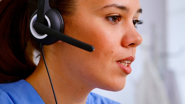 Close up of medical operator with headphone consulting patients during telehealth discussion in hospital. Healthcare physician in medicine uniform, doctor nurse assistent helping with appointment