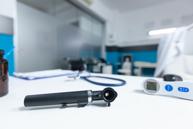 Close up of medical otoscop standing on table in empty doctor office during sickness consultation. Hospital workplace with nobody in it equipped with health care tools. Medicine concept