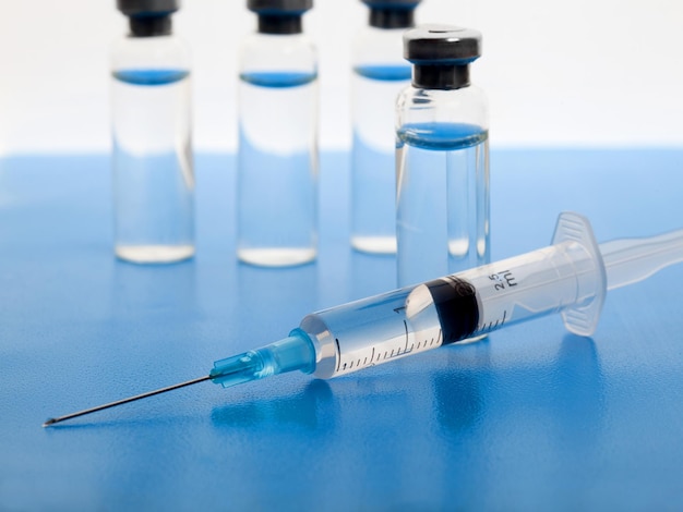 Close-up medical syringe and vials with medicine for injection. On white blue background