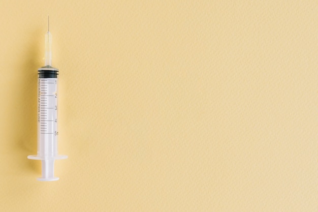 Close-up of medical syringe on yellow textured background