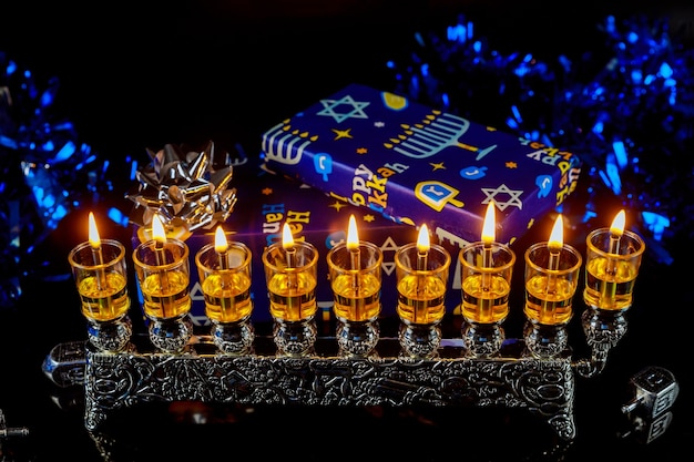 Close up of menorah with candles for Hanukkah and gift box on background. Jewish holiday.