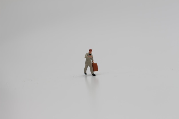 Photo a close up of a miniature figure of an office worker carrying a suitcase isolated on a white background miniature figure photo concept