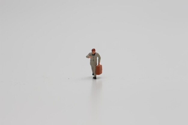 Photo a close up of a miniature figure of an office worker carrying a suitcase isolated on a white background miniature figure photo concept