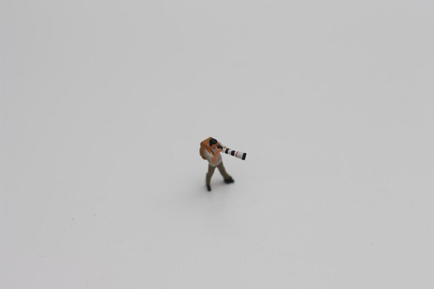 Photo a close up of a miniature figure of a photographer with a camera and telephoto lens isolated on a white background miniature figure photo concept