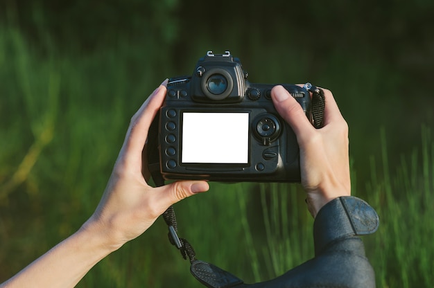 Close-up Mock-up of a professional photo-video camera in the hands of a girl. Against the background of green nature.