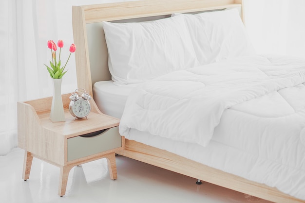 Close up of modern bed and bedside cabinet with clock and flower vase in the bedroom