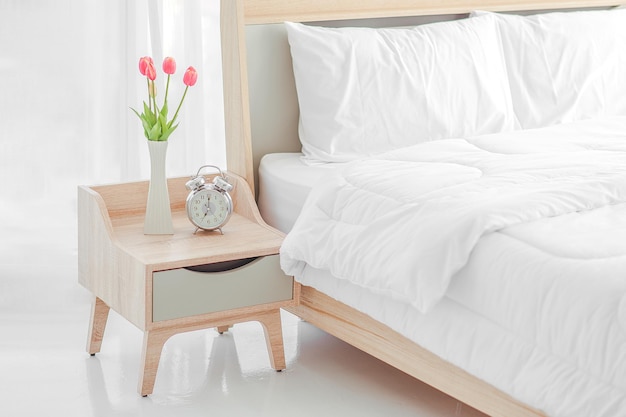 Close up of modern bed and bedside cabinet with clock and flower vase in the bedroom