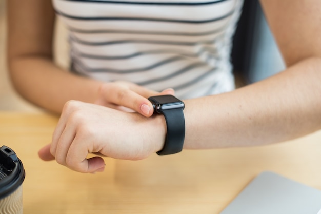 Close up of a modern black smartwatch being on the wrist of a beautiful young woman