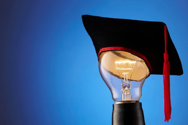 Close-up of mortarboard on illuminated light bulb against blue background