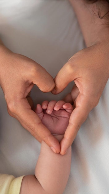 Close up mother holding hands newborn boy and giving heart signal in a room