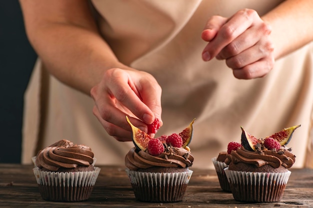 Close up of muffin preparation Pastry chef decorates cupcakes with raspberries and figs