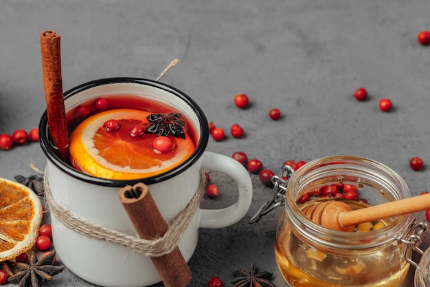 Close up of mulled wine cup with spices and berries on grey table