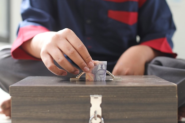 Close up of Muslim child hands put money into a charity box for donation Helping each other and sup