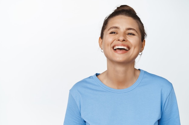 Close up of natural young woman laughing and smiling, model has white healthy teeth and happy face expression, wears blue t-shirt, studio