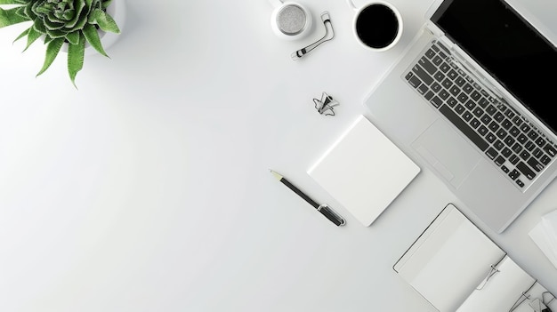 close up of office desk with laptop and stationery featuring a black keyboard and a green plant on the left against a white wall