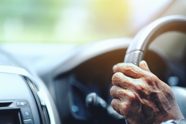 Close up old man driver keeps hands on the steering wheel