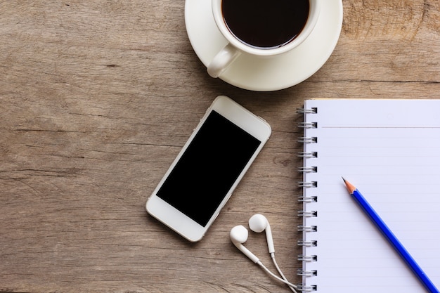 Close up of old wooden desktop with notebook, smartphone, coffee cup, earphones 