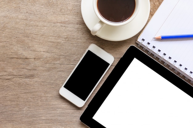 Close up of old wooden desktop with tablet, smartphone, coffee cup, notebook and pencil.