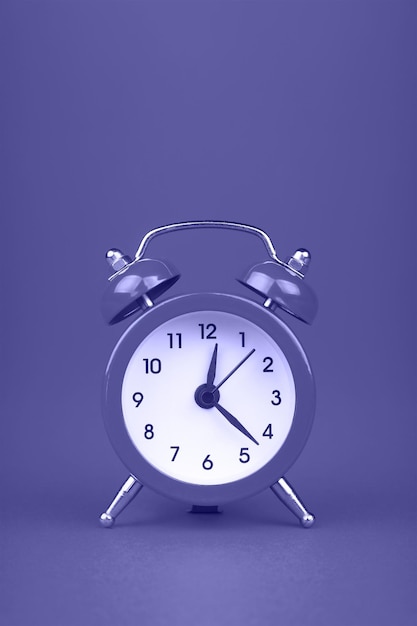 Close up one small purple metal twin bell retro alarm clock over violet background with copy space, very peri, color of year 2022