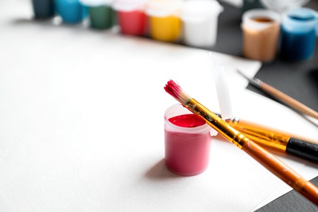 Close up paintbrush lean on plastic jar with red gouache paint