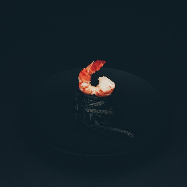 Photo close-up of pasta with prawn in plate on table against black background